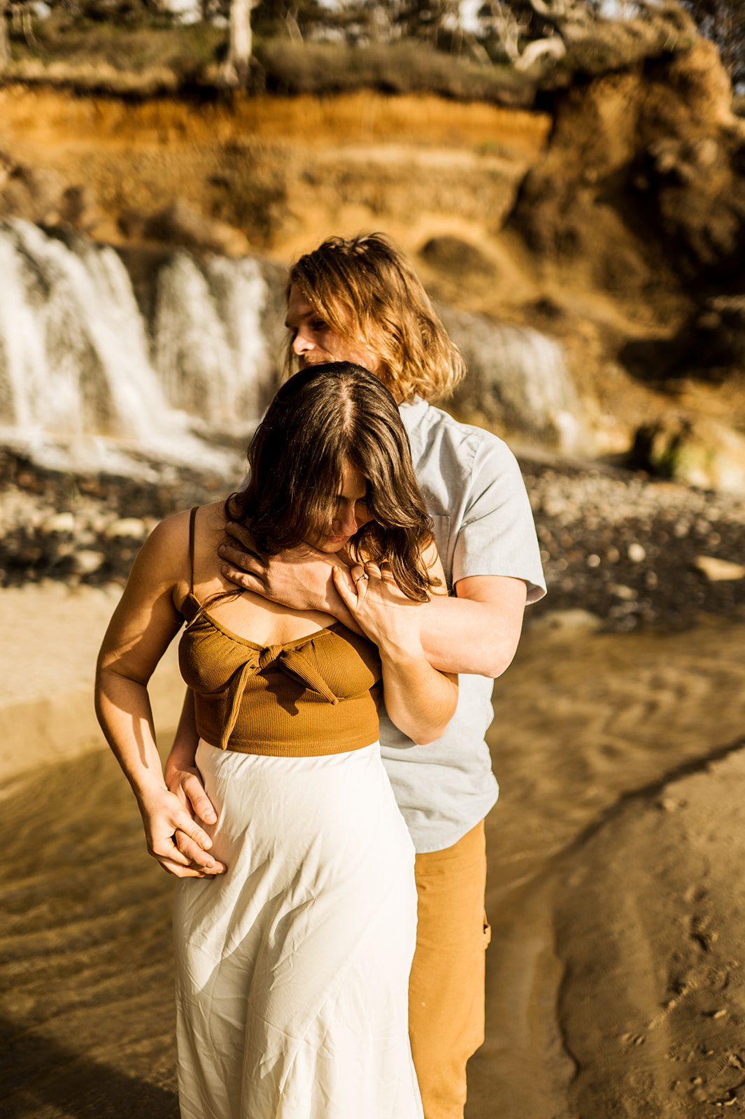 cannon beach oregon engaged couple stands in front of hug point waterfall at sunset