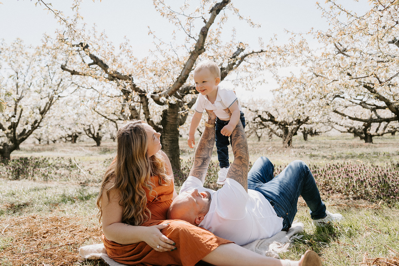 Parents sitting on the ground while dad holds toddler above his head.