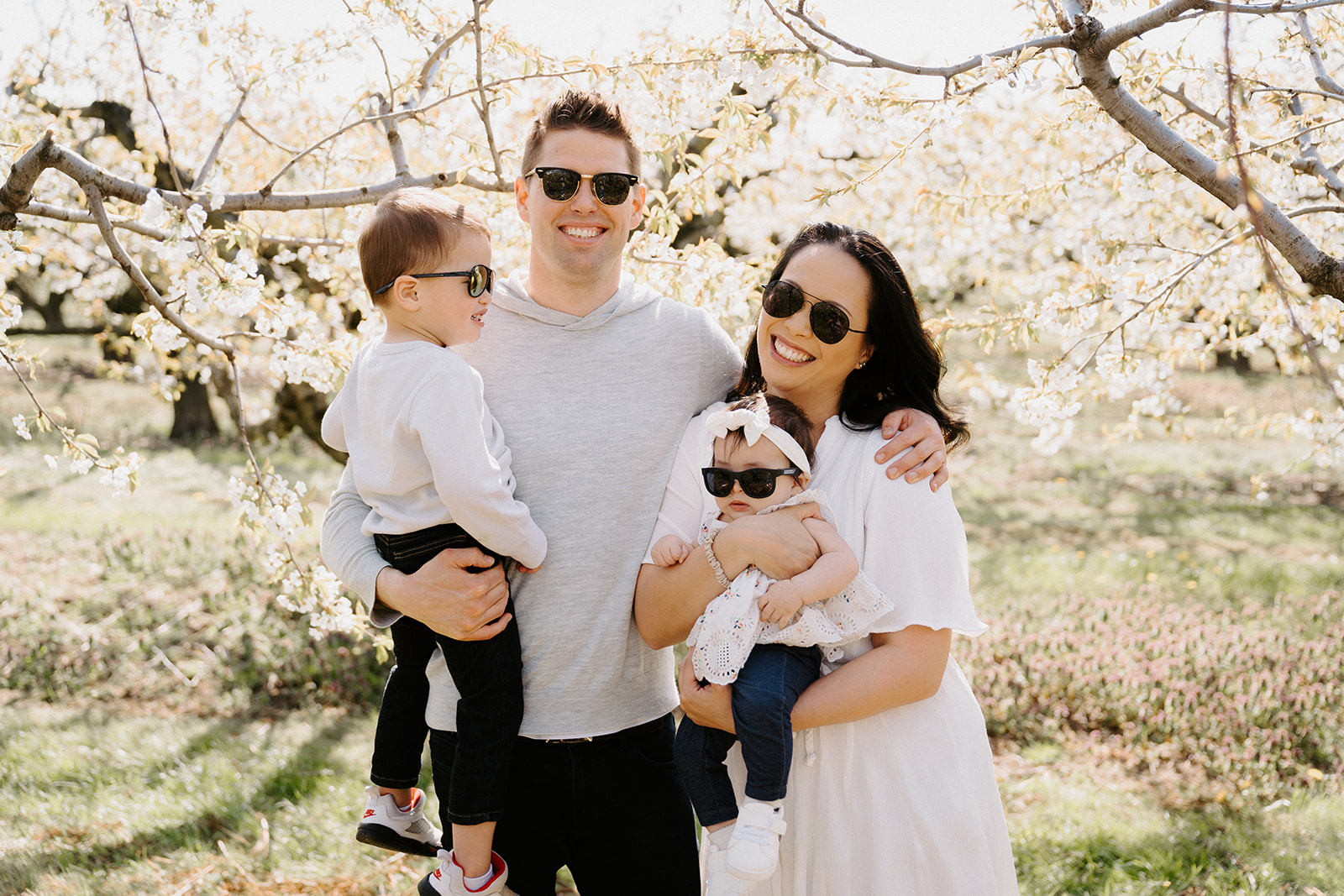 Family of four standing underneath cherry blossom trees with sunglasses on.