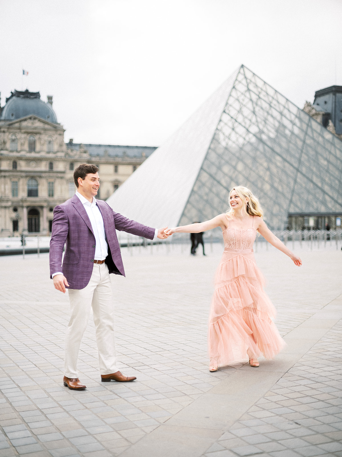 Man spins woman in front of the Louvre.