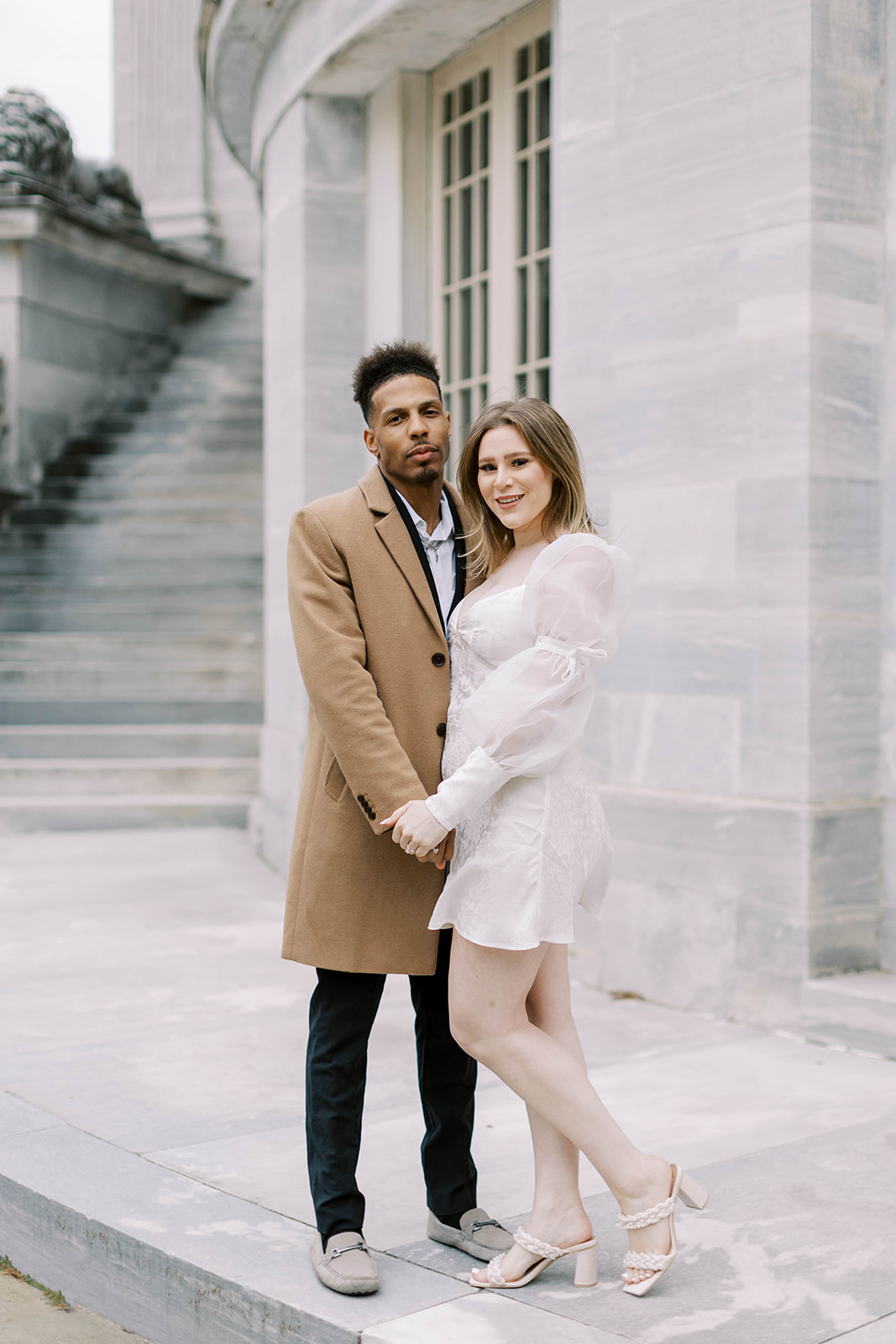 Couple holds hands and smiles at the camera during their engagement session in city hall Philadelphia.