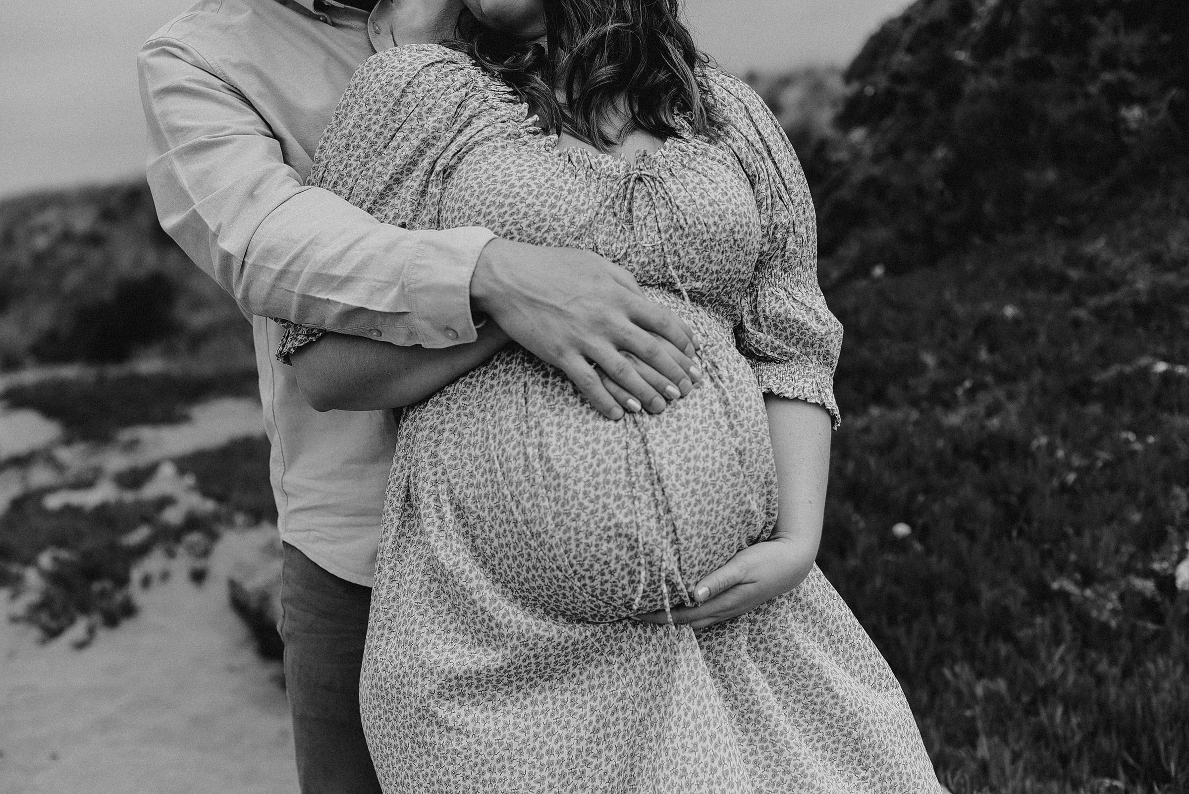 a couple expecting a child in Fort Bragg, California holding their pregnant belly on the sandy beach.