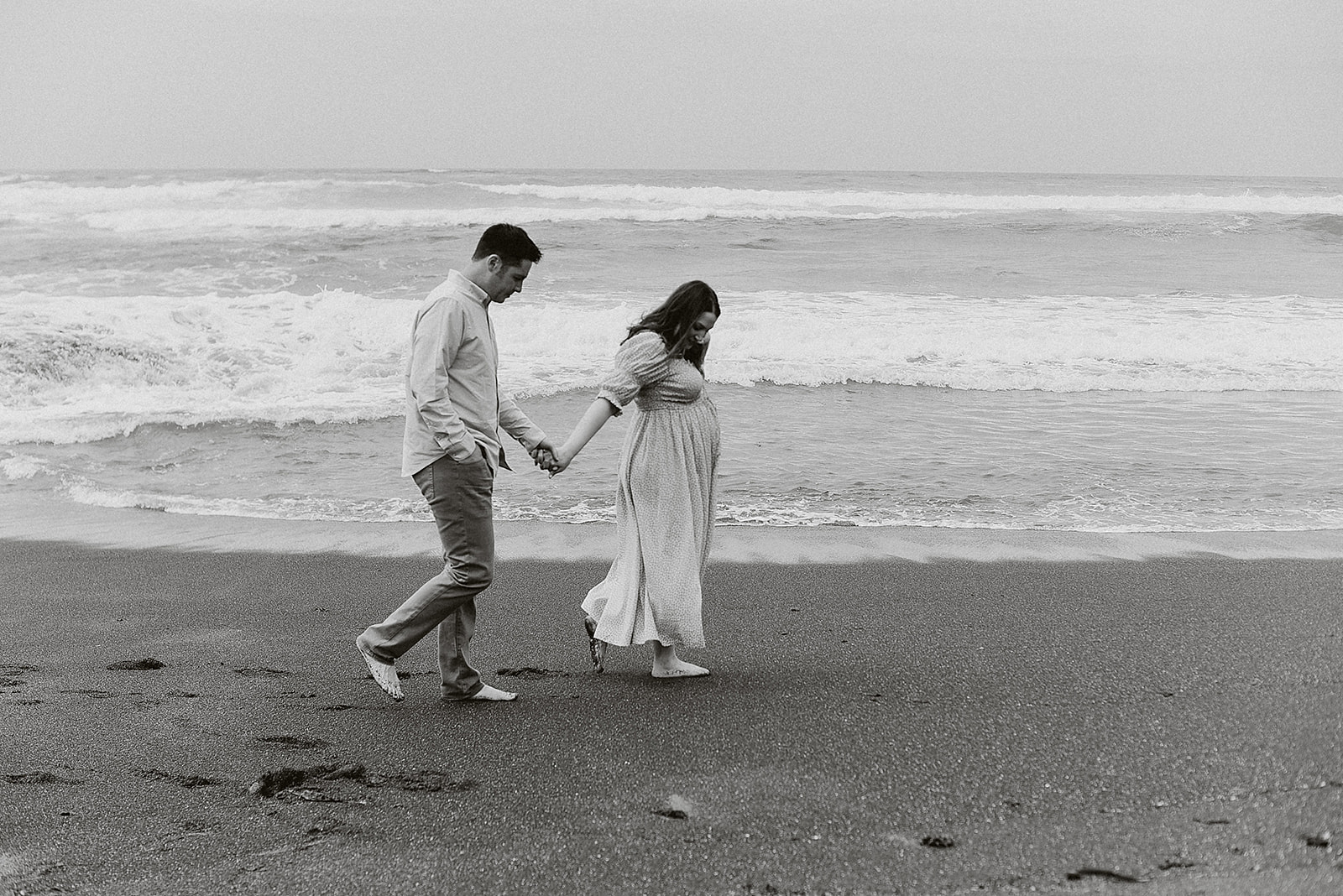 a couple holding hands and walking down the beach during their romantic maternity session in Fort Bragg California.