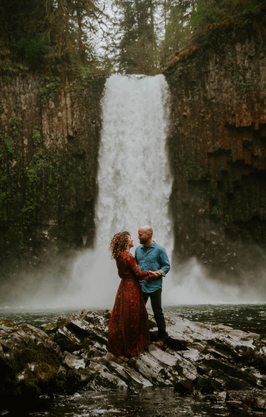 Man dipping his fiancé in front of a waterfall and kissing her neck and chest. 