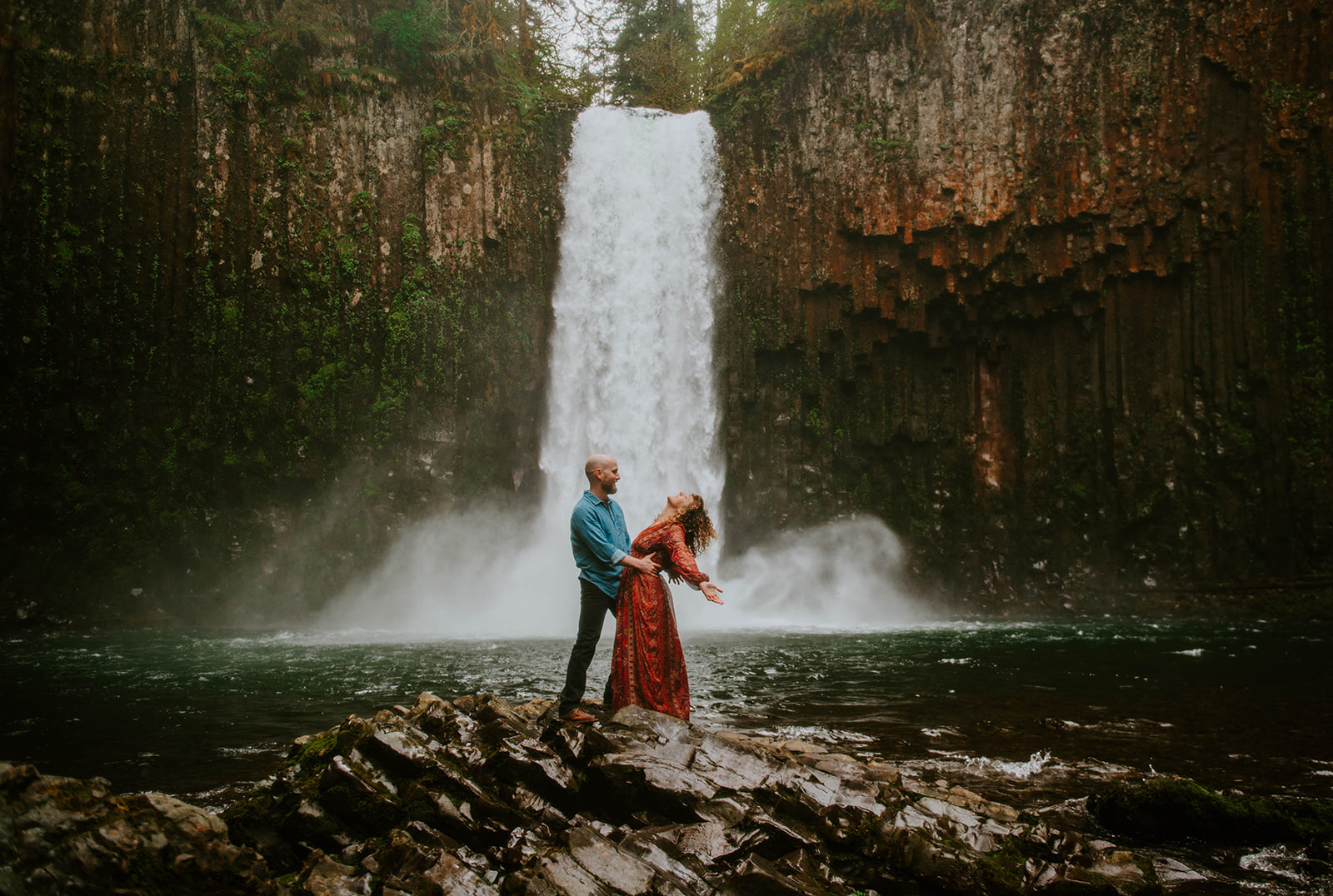 Man holding woman while she leans backwards in a red dress at Abiqua Falls