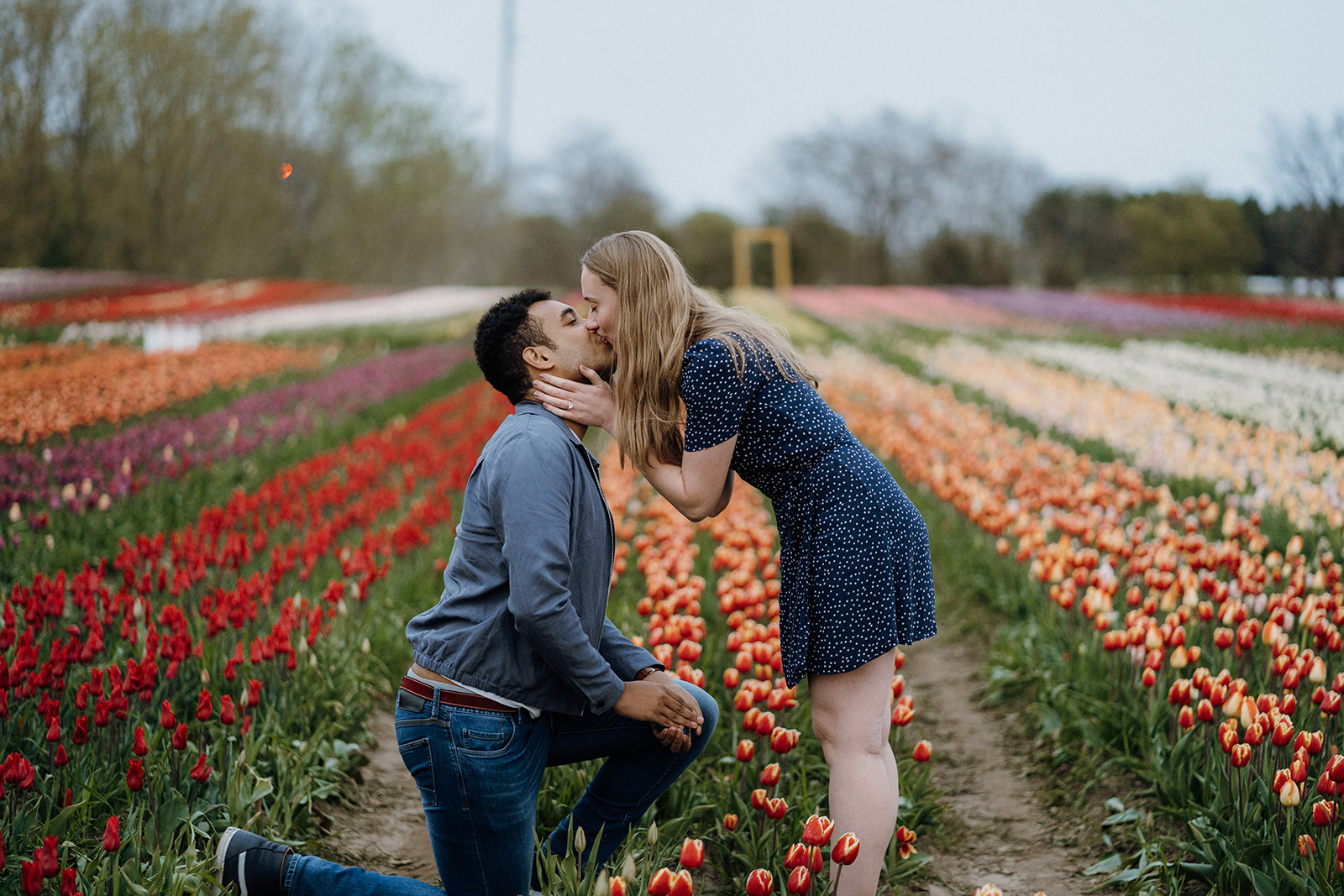 Man kneeling in tulips while his girlfriend bends down to kiss him.