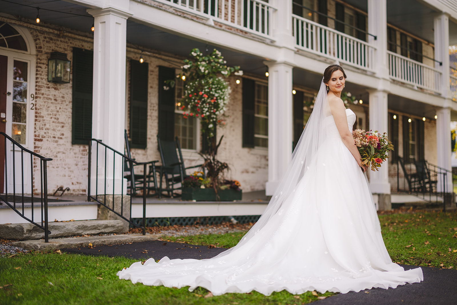 a bride in a white gown holding her flowers poses in front of the historic Grafton Inn in Grafton Vermont