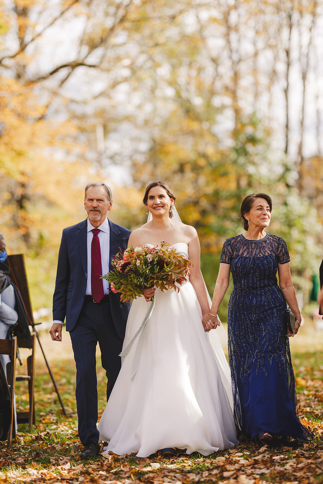a bride in a white wedding gown is walked down the aisle by her parents at an outdoor wedding in the fall