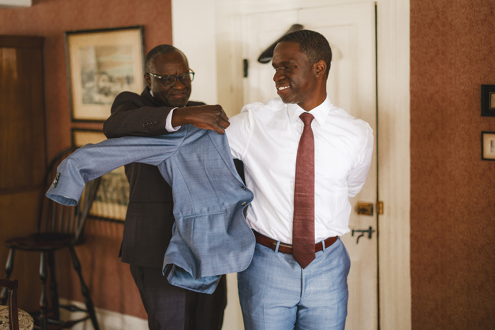groom's father helps his son get ready for wedding by putting his jacket on