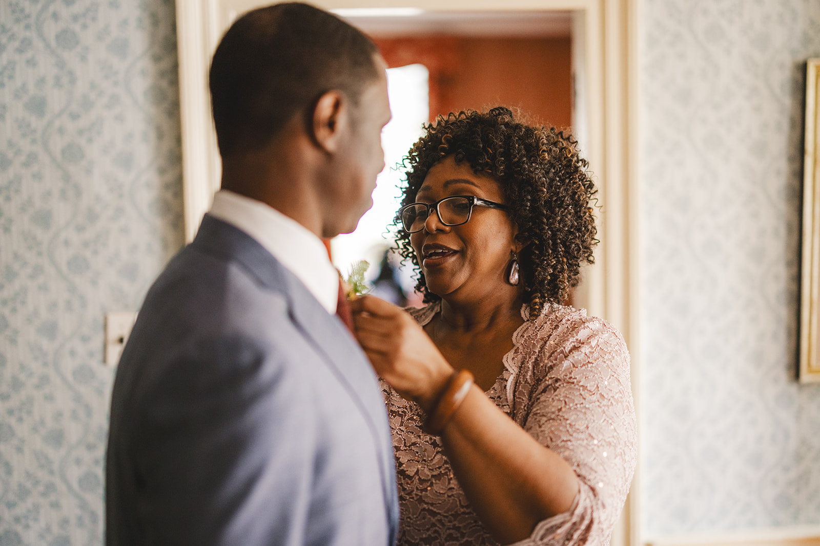 groom's mother helps her son get ready for wedding by attaching his boutonniere 