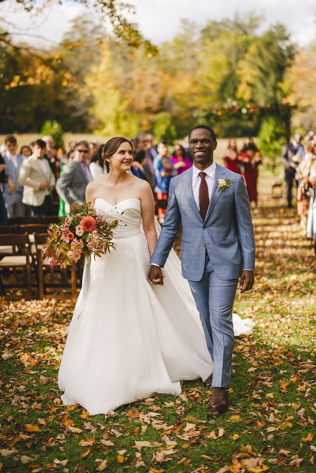 a smiling bride and groom walk together after their outdoor fall wedding ceremony