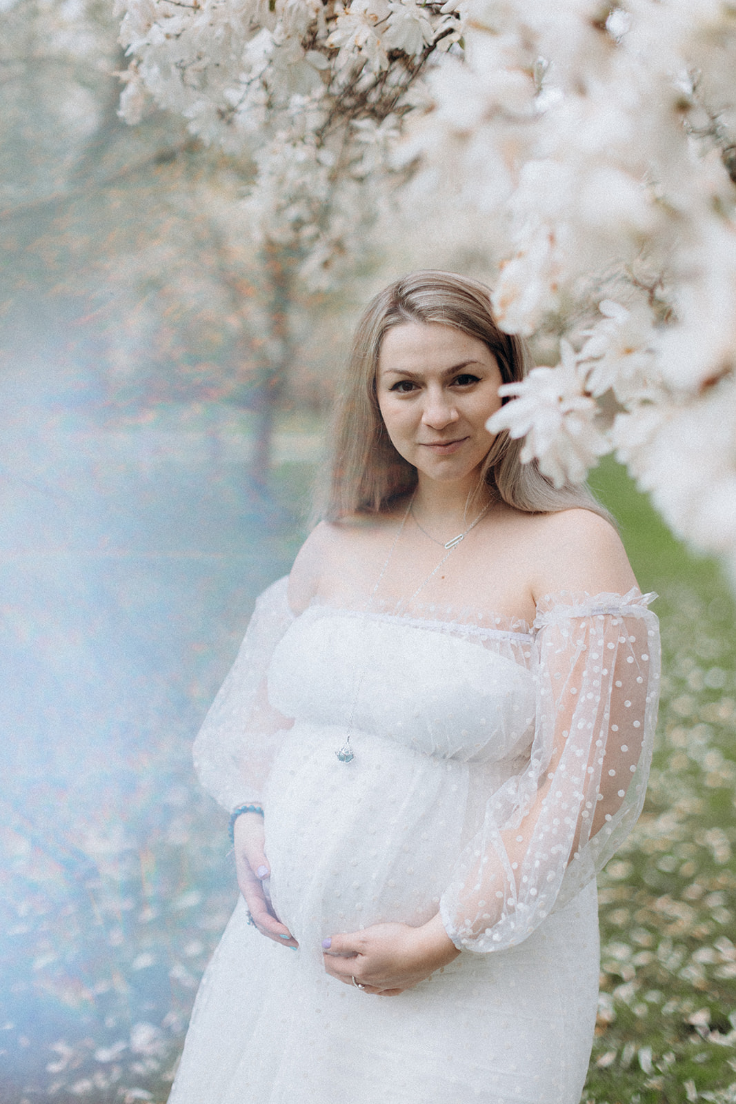 White blooming magnolias framing maternity portrait of pregnant girl in white dress