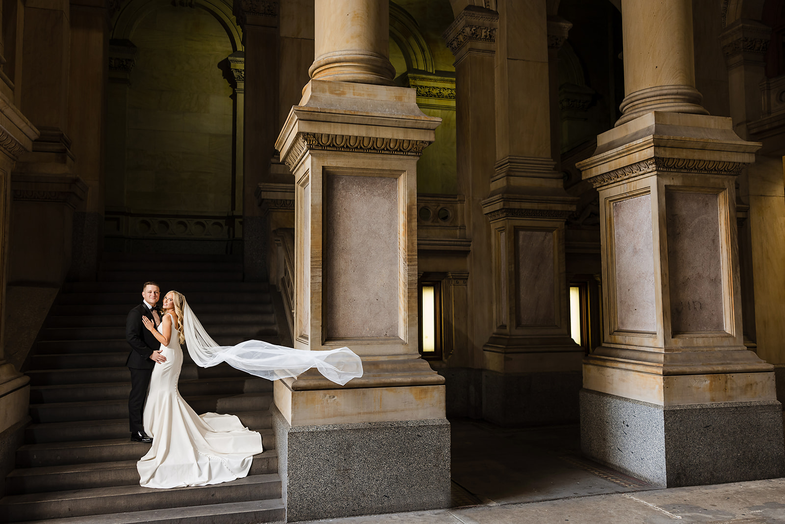 Dramatic photo of the bride and groom with flowing veil on the steps of Philadelphia City Hall