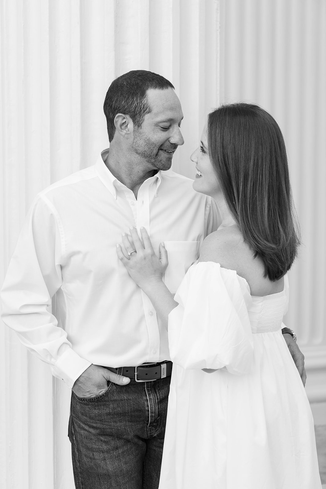 A black and white image of a beautiful couple snuggled up against a white column