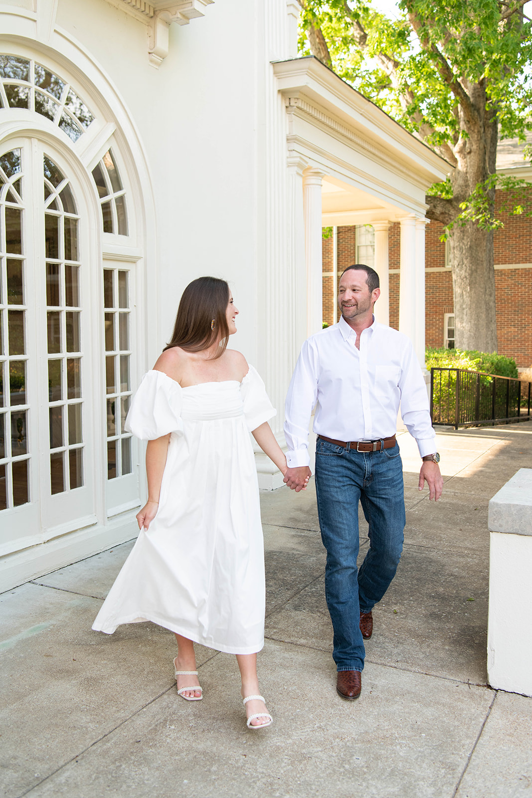 Bride to be wears a white off the shoulder dress and groom to be wears a white button up shirt and blue jeans