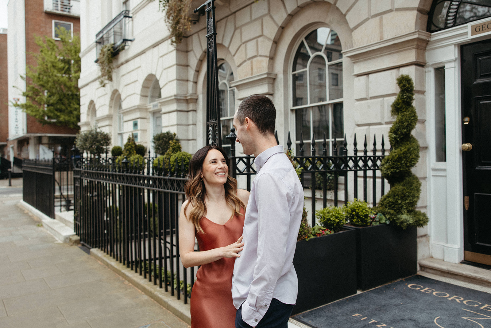 A luxury engagement session couple admires one another while standing in front of George House in Fitzroy Square, London