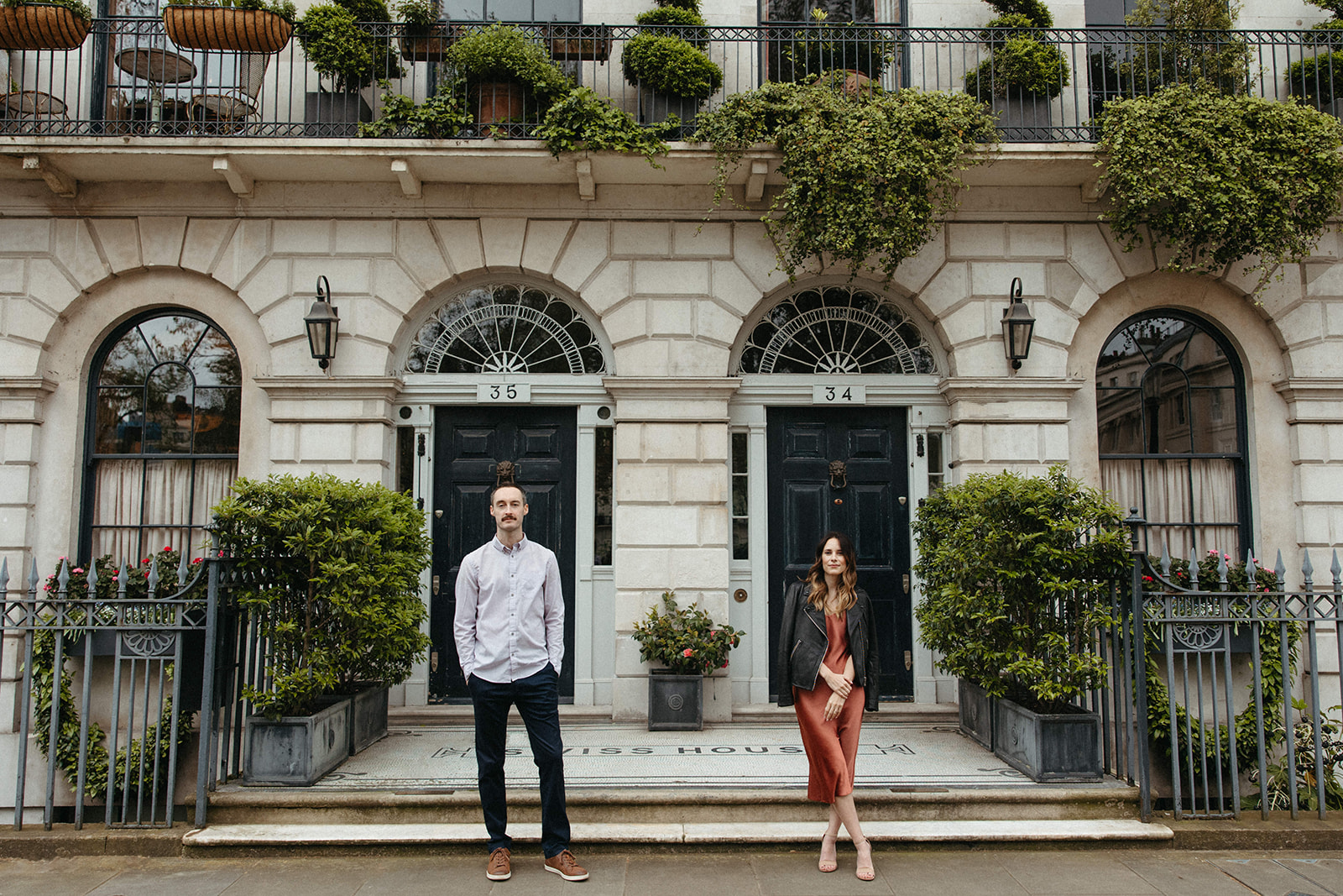 A man and woman stand in front of Swiss House in London while wearing elevated engagement outfits. 