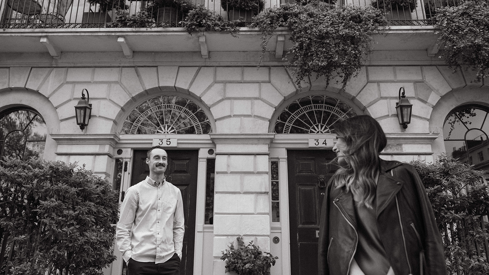 A candid engagement session photo of a man and his fiancée in front of a historic brick building in London. 
