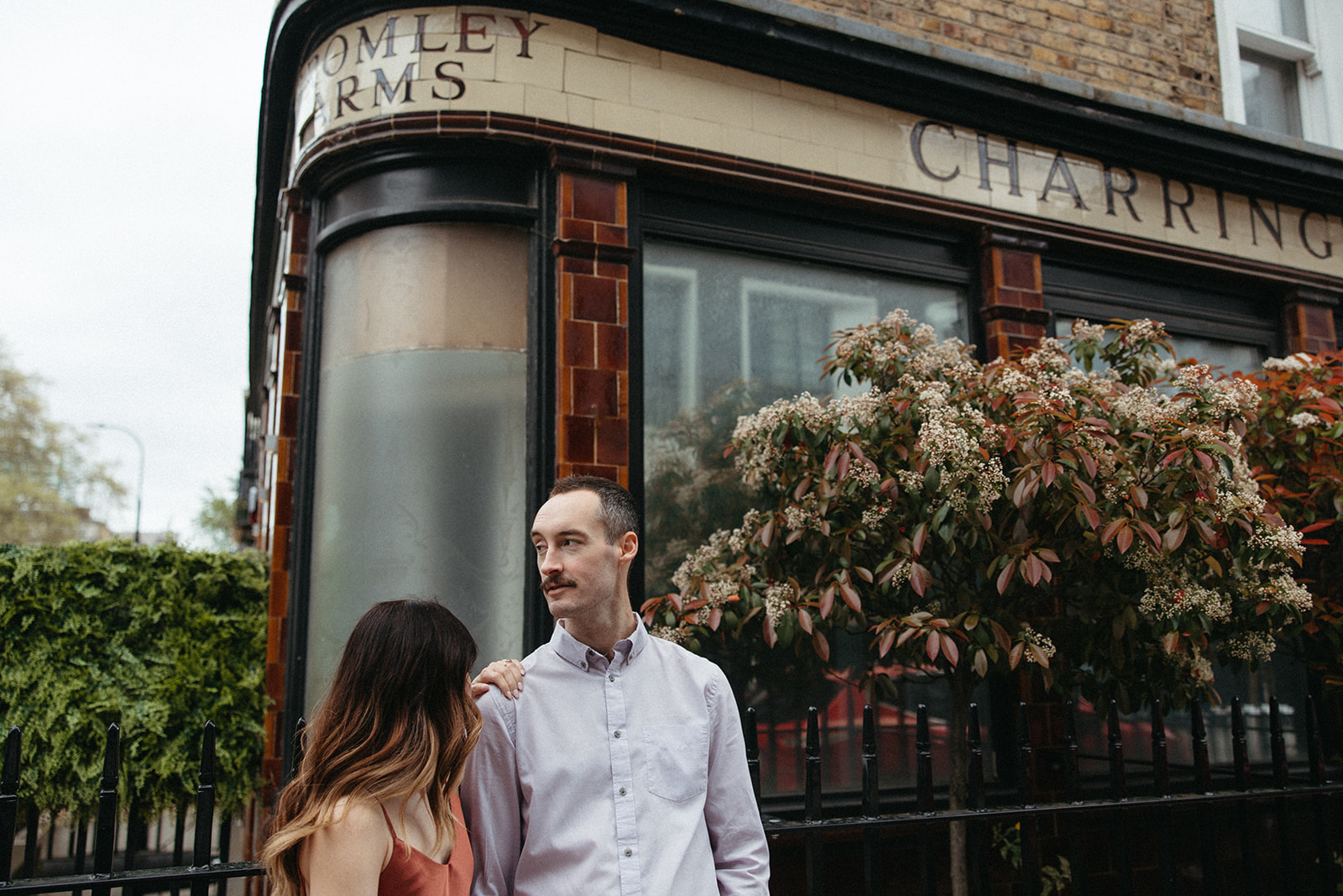 A man looks out onto a London street while standing next to his fiancée during their luxury engagement session. 