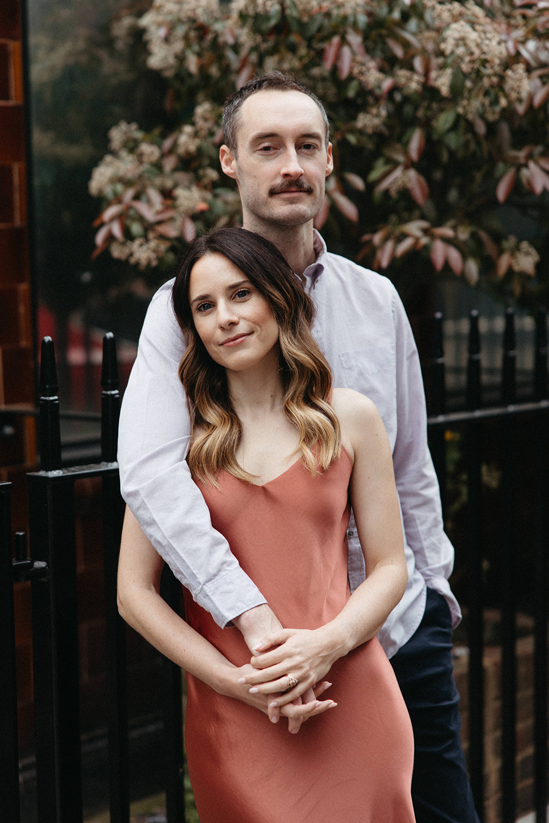 An engaged couple embraces near a black, wrought iron fence in London for their city engagement session in England. 