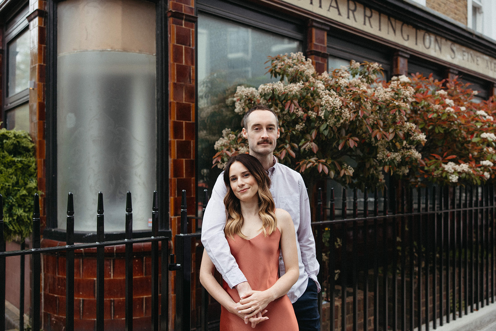 A couple softy smiles at the camera while embracing during their old money aesthetic engagement session in London. 