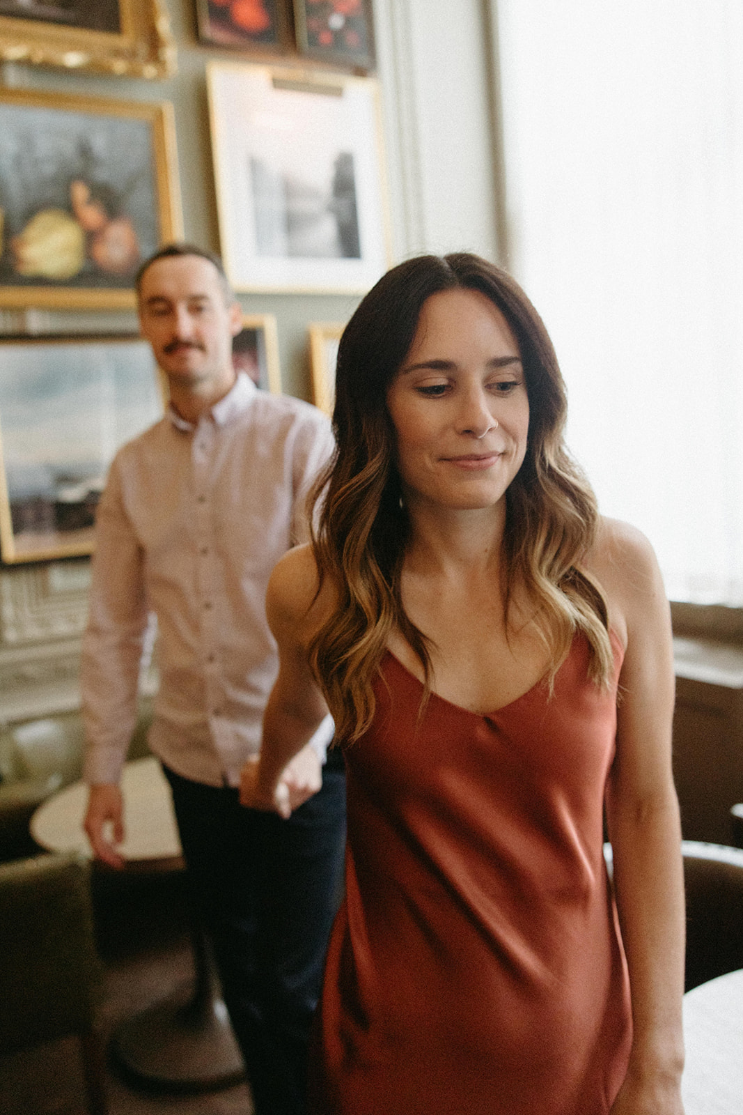 A woman leads her fiancé through Berner’s Tavern in London, which is decorated with vintage artwork in golden frame. 
