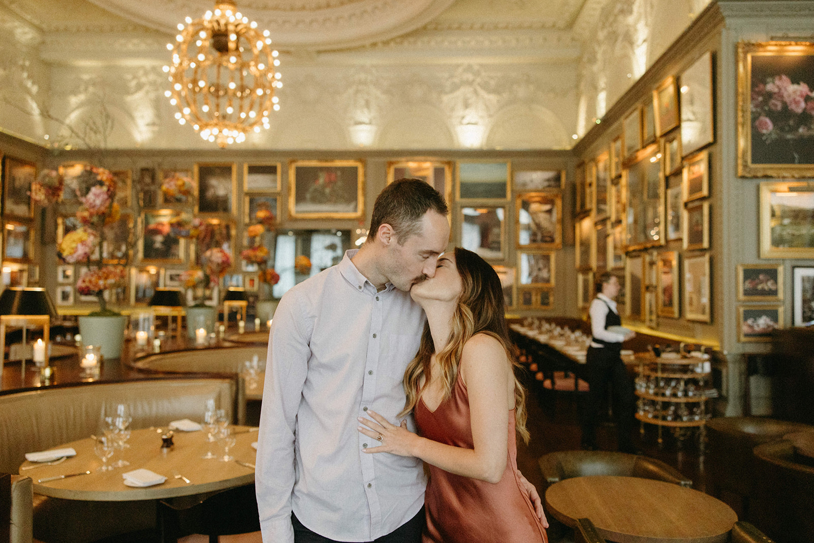 An engaged couple shares a kiss in a contemporary British restaurant during their city engagement session in London. 