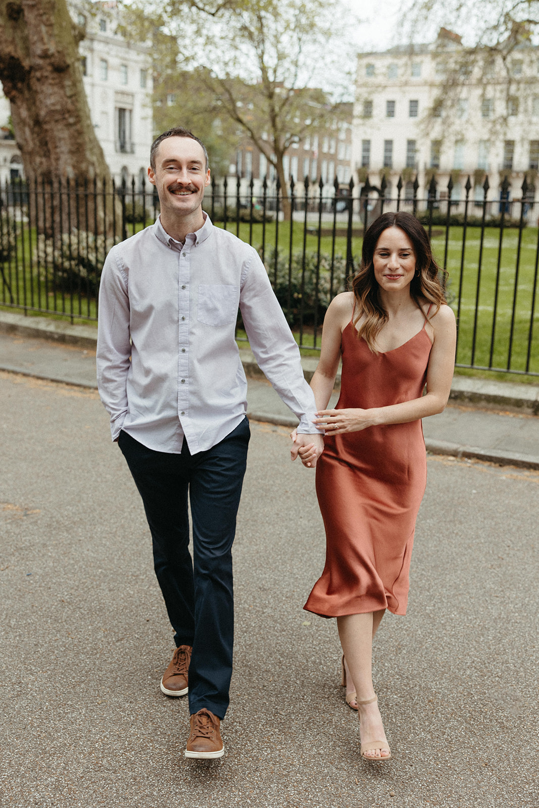 A couple who recently got engaged holds hands while walking during their London engagement session. 