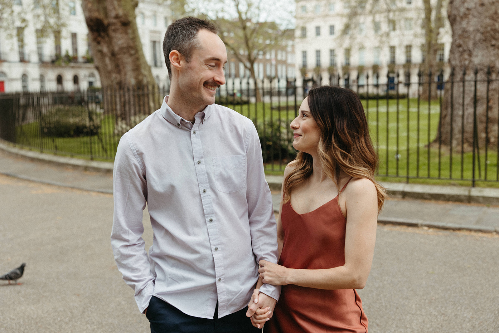 A couple admires one another along a city street during their old money aesthetic engagement session in London. 
