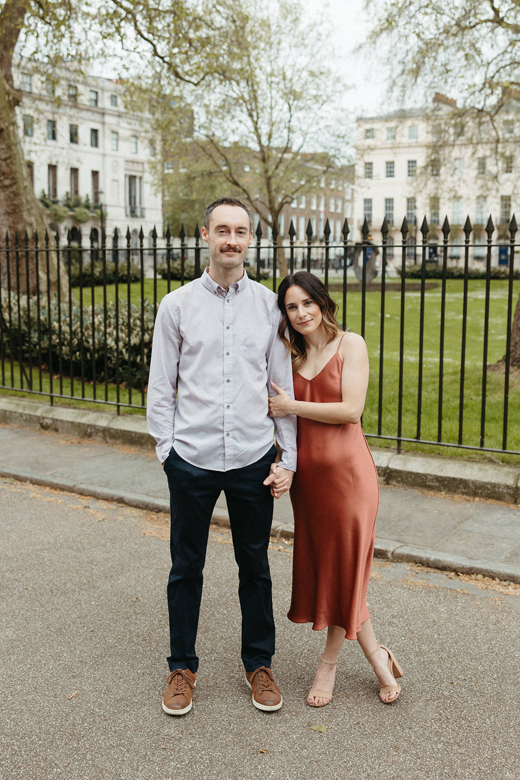 A woman wearing a hand-made satin dress leans against her fiancé during their London engagement session. 