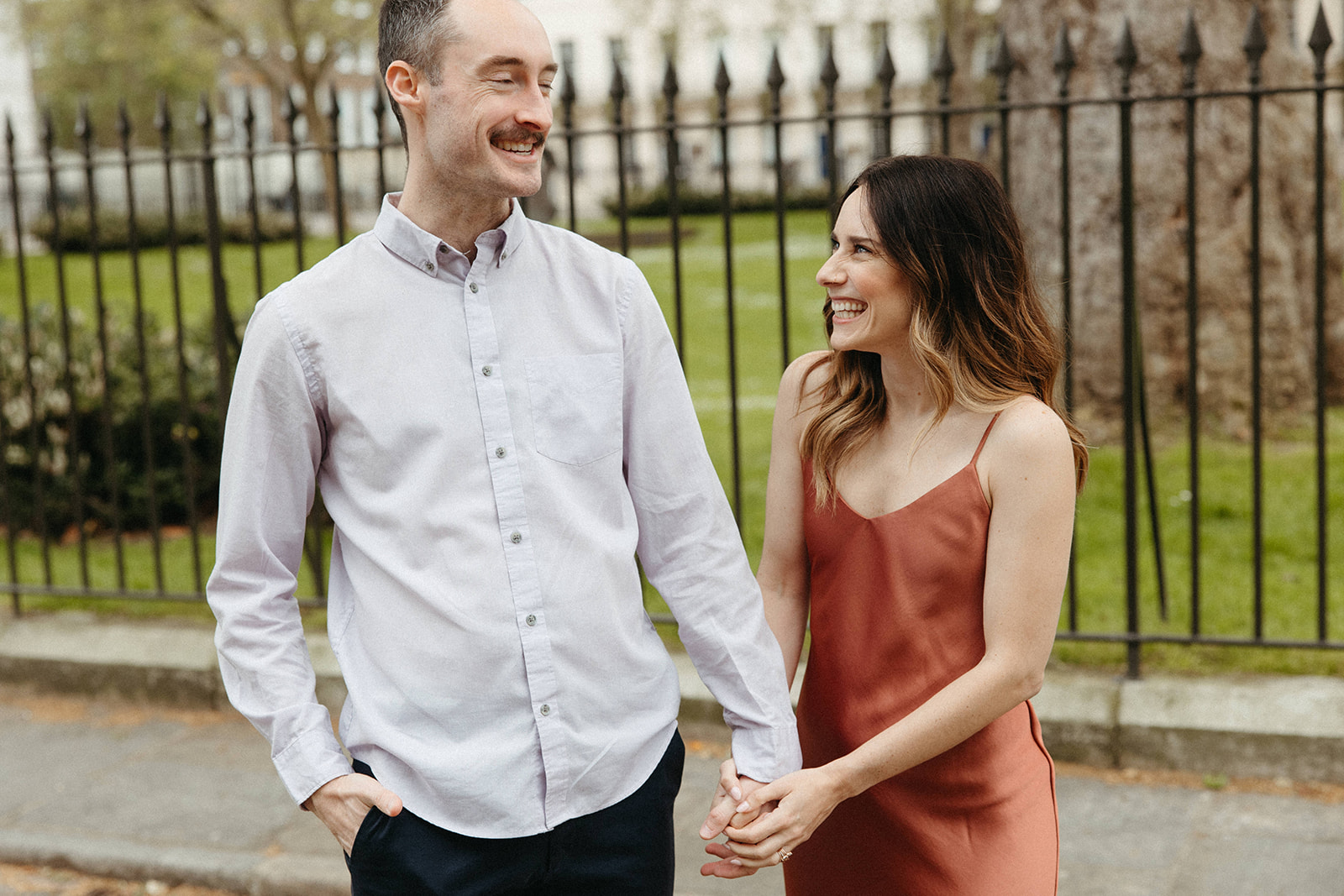 A newly engaged couple wearing elegant yet casual engagement outfits holds hands while walking through London, England.