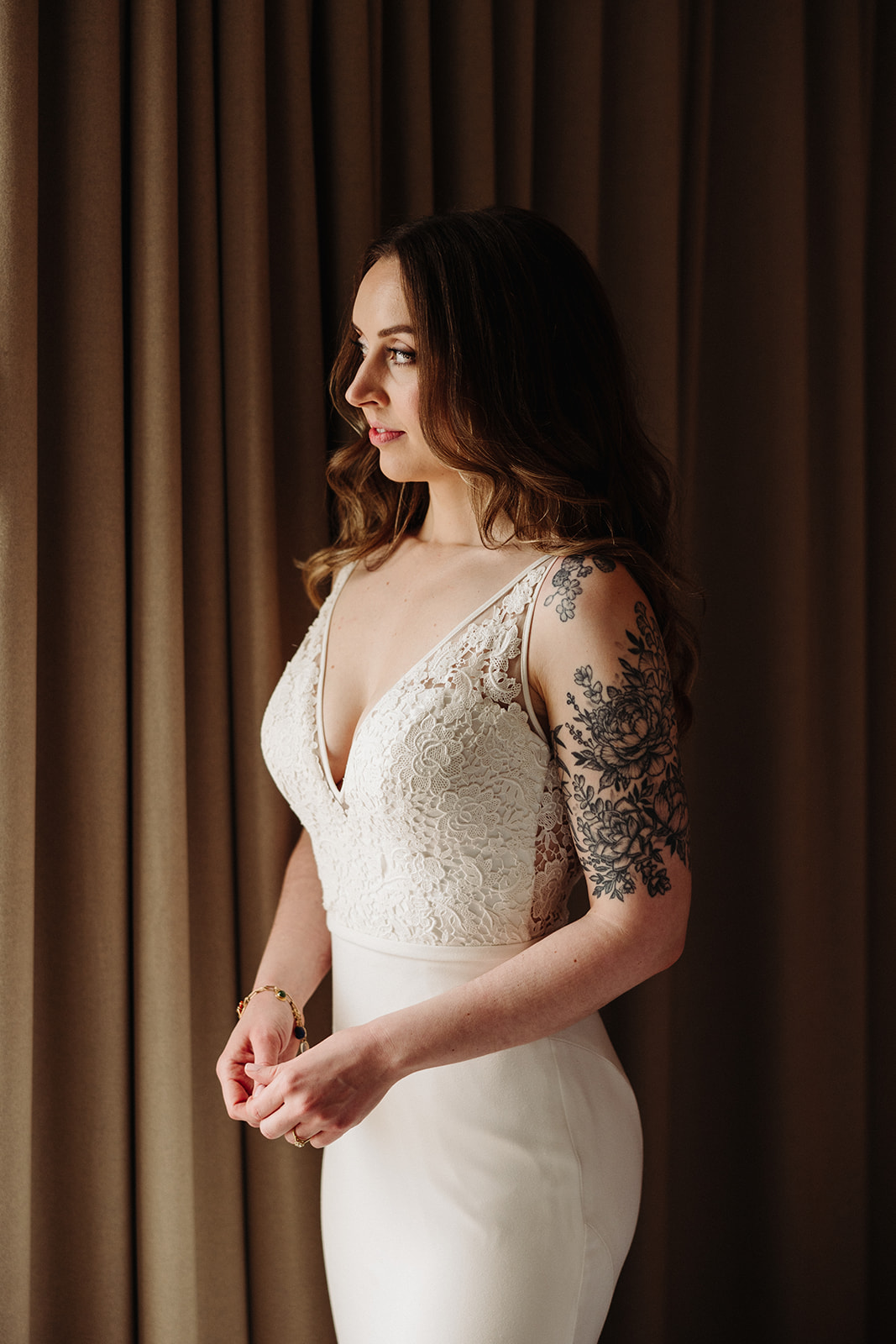 Woman looking out of a window wearing a lace bodice, mermaid wedding dress