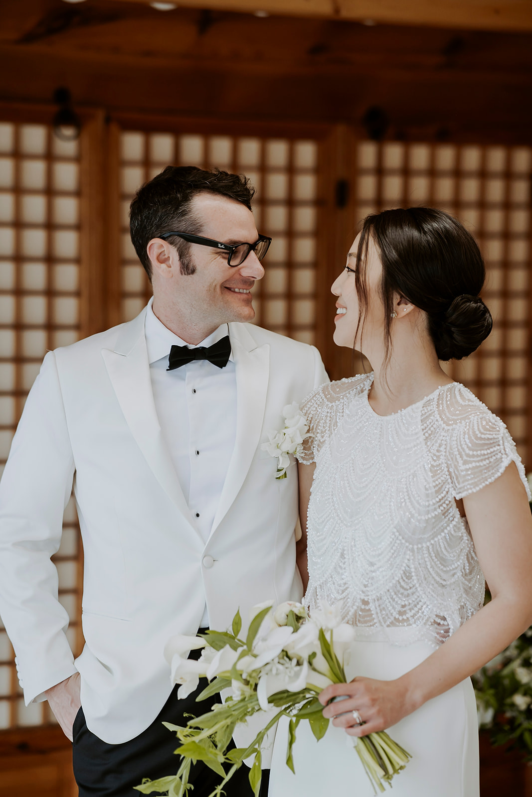 A bride in a beaded two piece dress and groom in a white tuxedo.