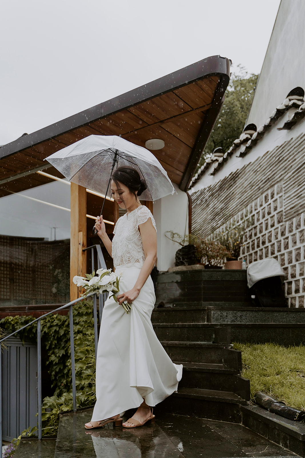 A bride in a beautiful white dress holding an umbrella for her hanok wedding.