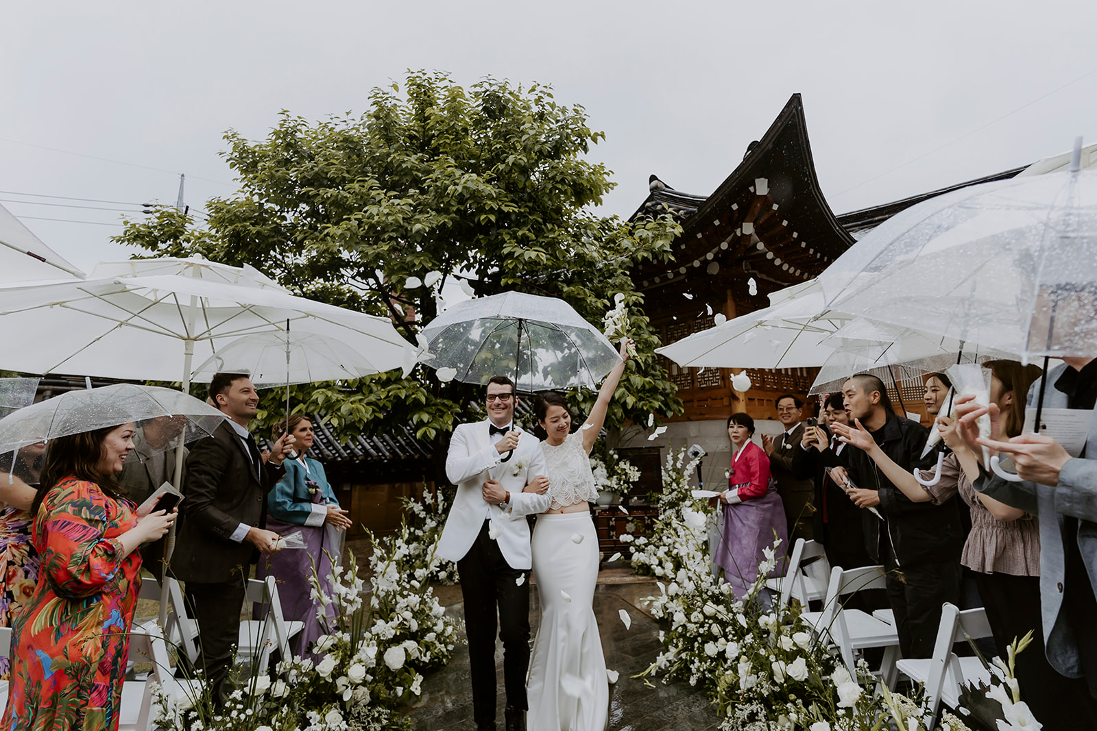 A couple is holding umbrellas during their hanok wedding ceremony.