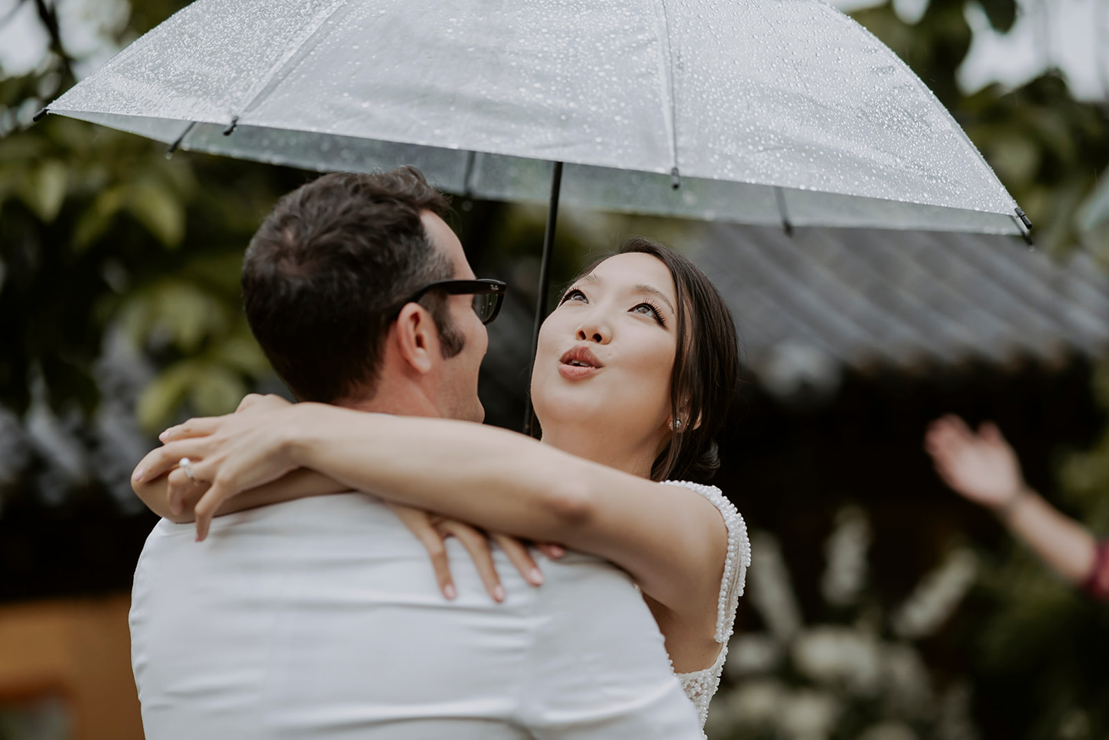 A hanok wedding with the bride and groom hugging under an umbrella.