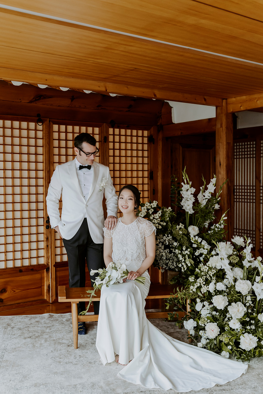 A man and woman in a traditional hanok posing in their wedding attire.