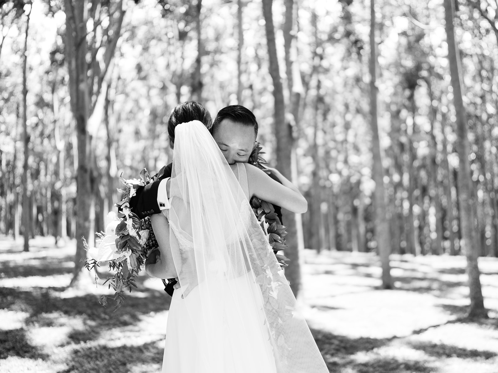 Black and white photo of a  Bride and groom embracing in a forest setting captured by Oahu Wedding Photographer