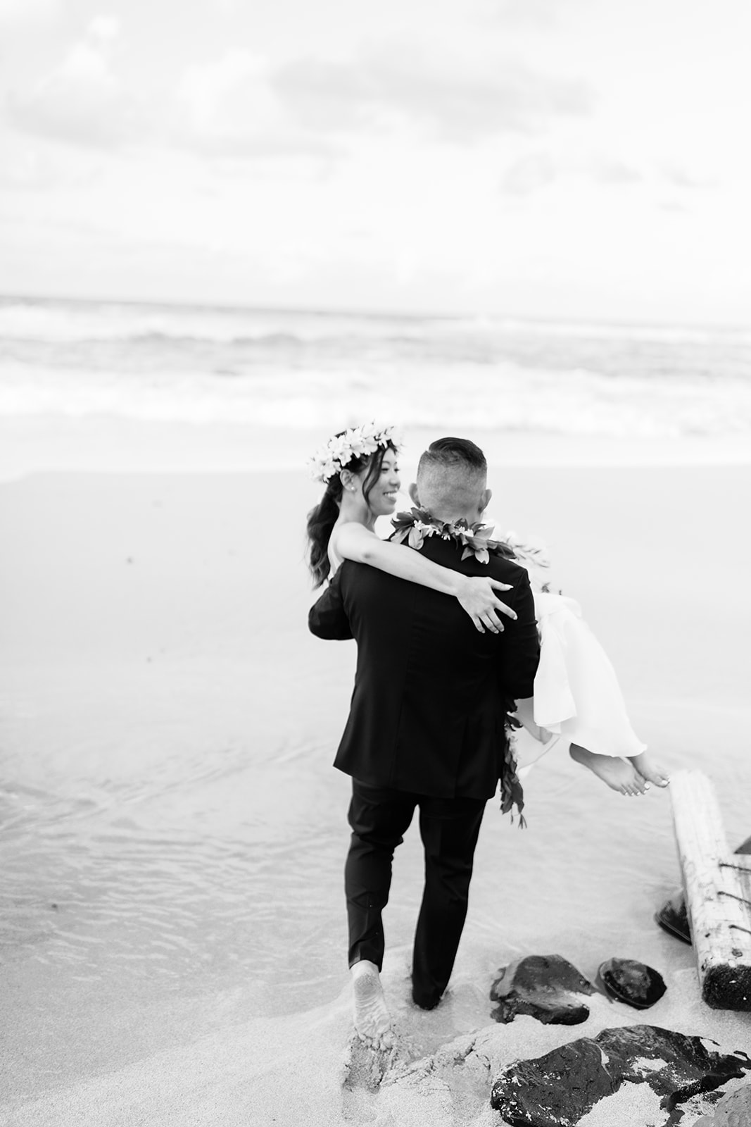 Black and white photo of a groom carrying bride on a sandy beach captured by Oahu Wedding Photographer
