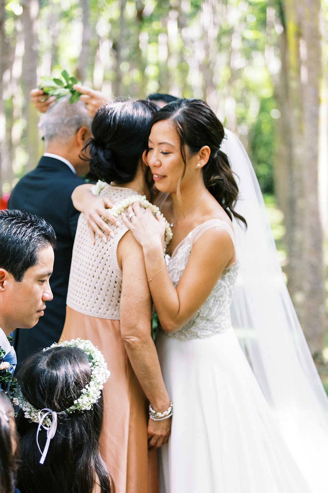 A bride embracing her mother at a wedding ceremony amidst a wooded setting captured by Oahu Wedding Photographer