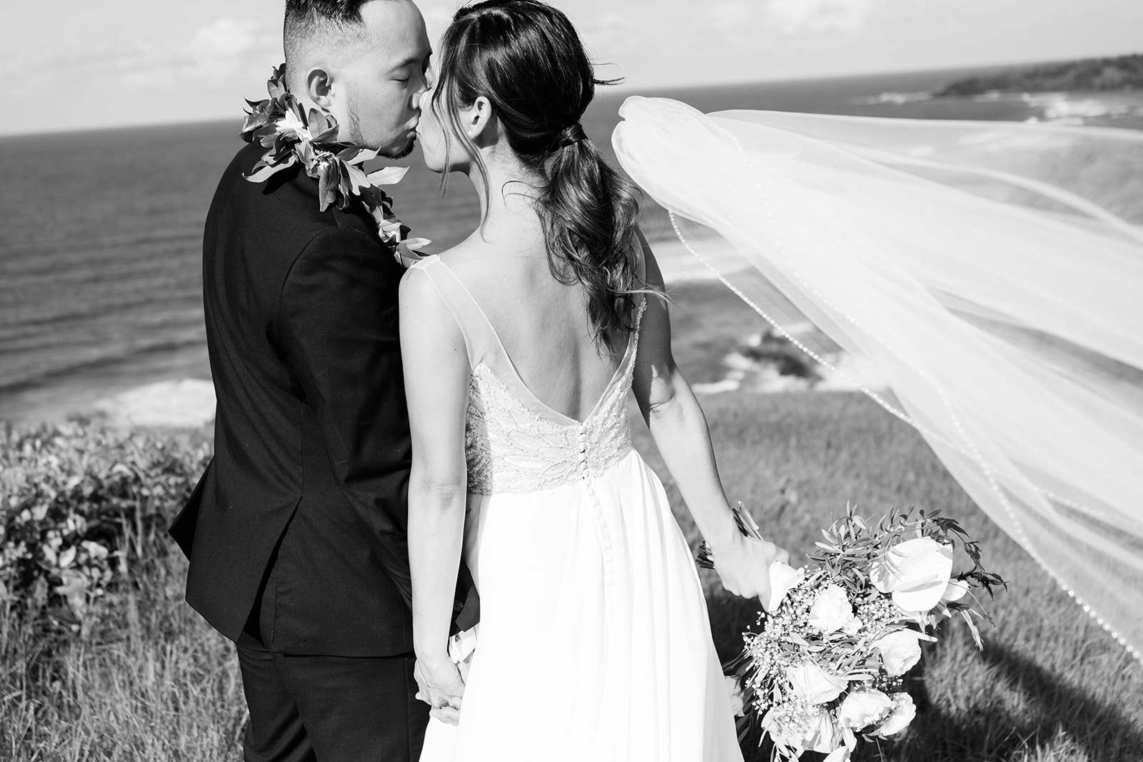 A bride and groom having an intimate moment on a grassy overlook with a coastal backdrop Wedding at Na Aina Kai