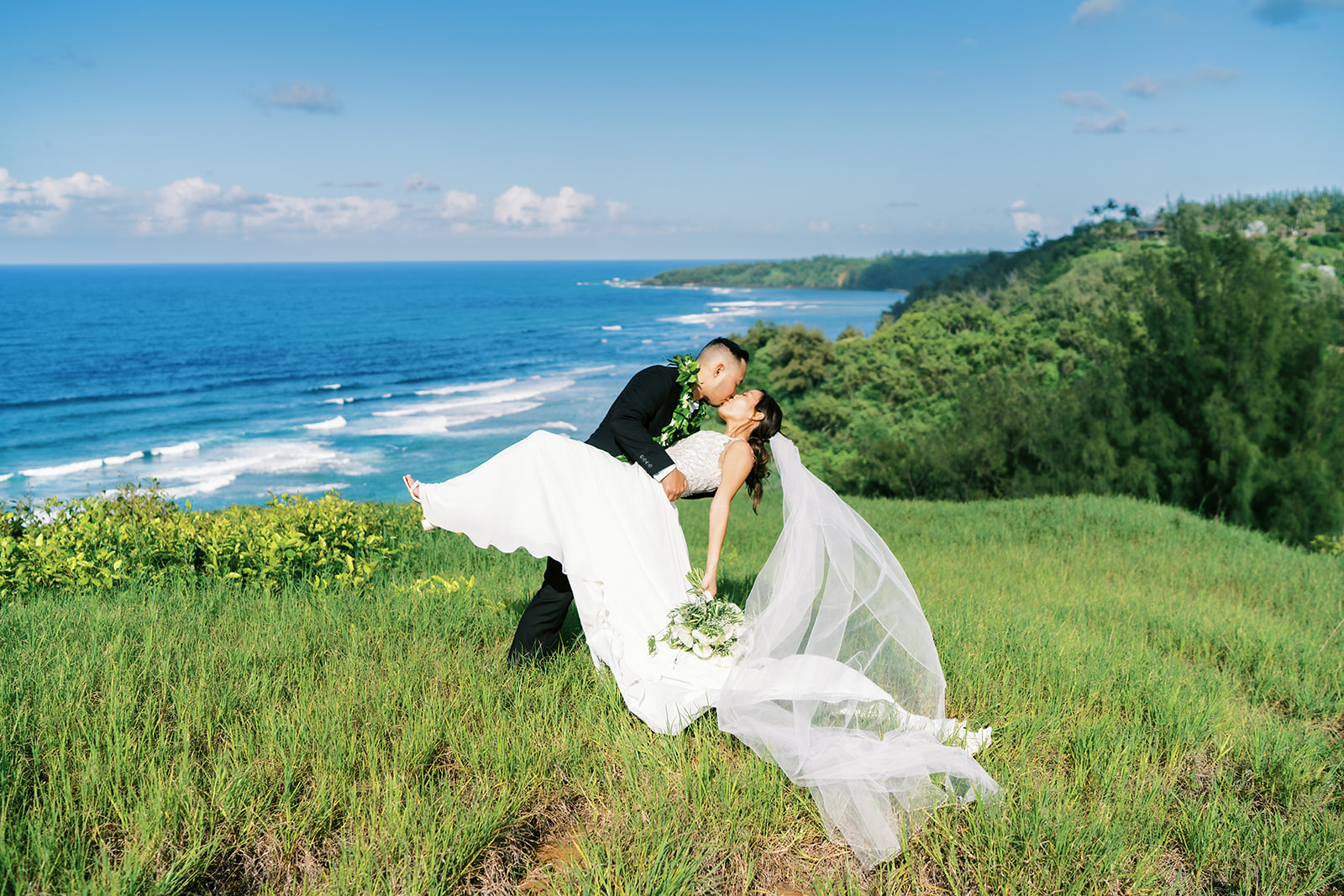 Bride and groom sharing a kiss on a lush coastal hillside captured by Oahu wedding photographer.