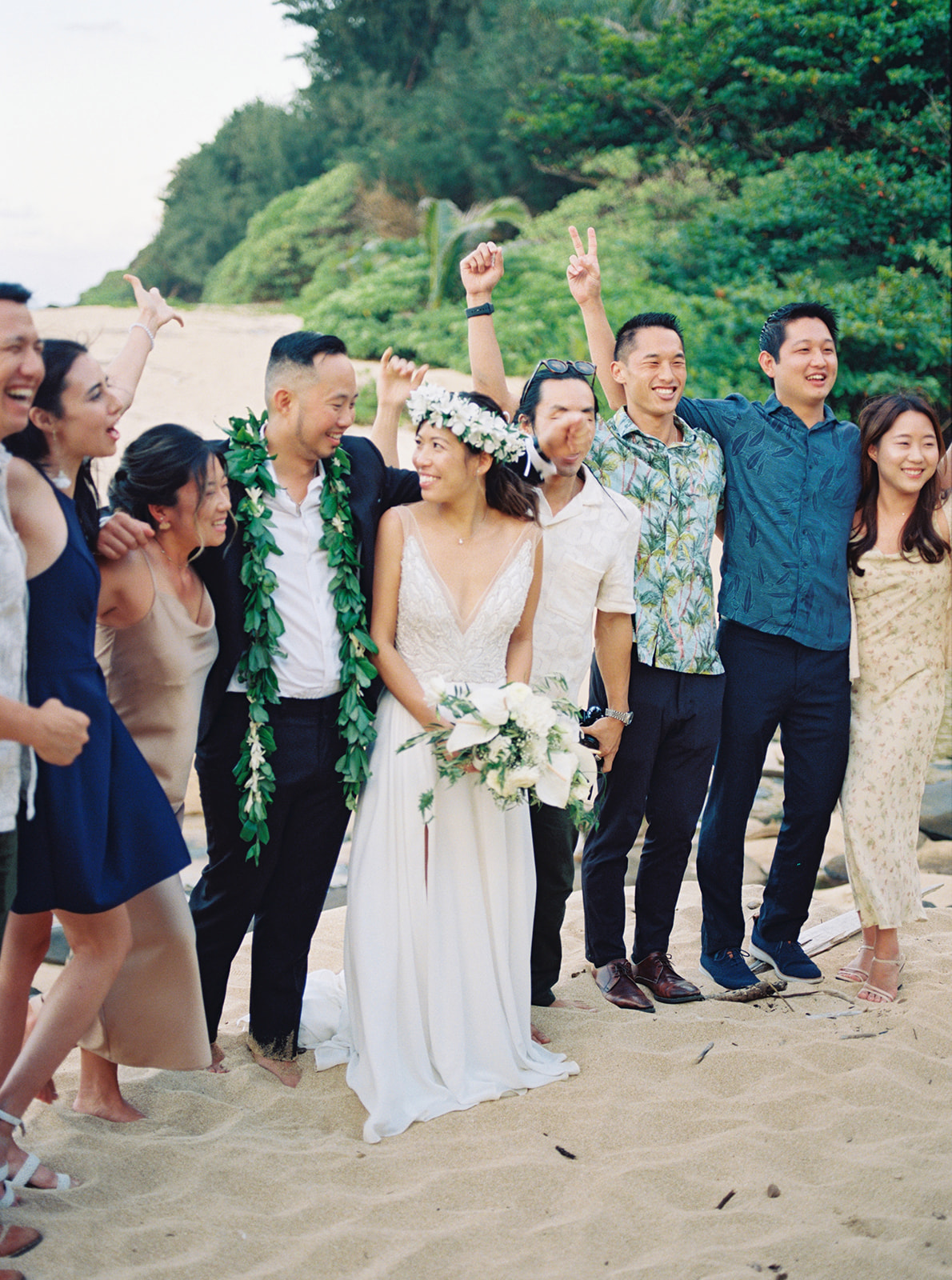 Bride and Groom walking on a beach with some of their wedding guests taken by Oahu Wedding Photographer at Na Aina Kai