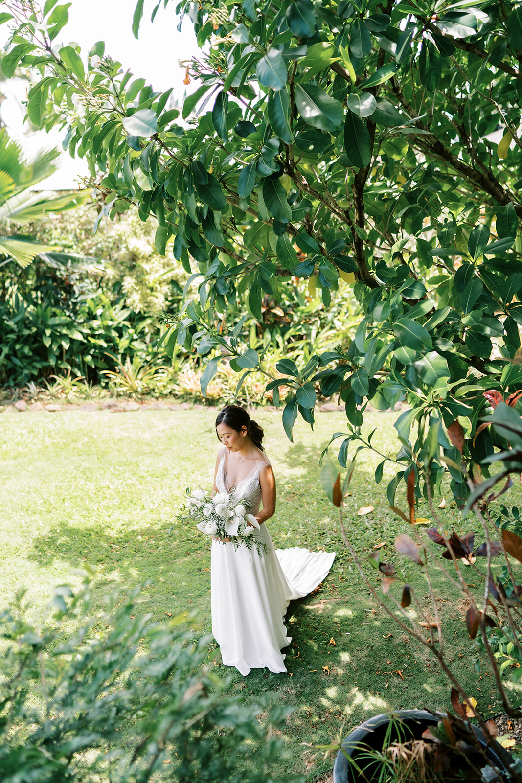 Bride holding a bouquet while standing amidst lush greenery at Na ‘Āina Kai Botanical Gardens
