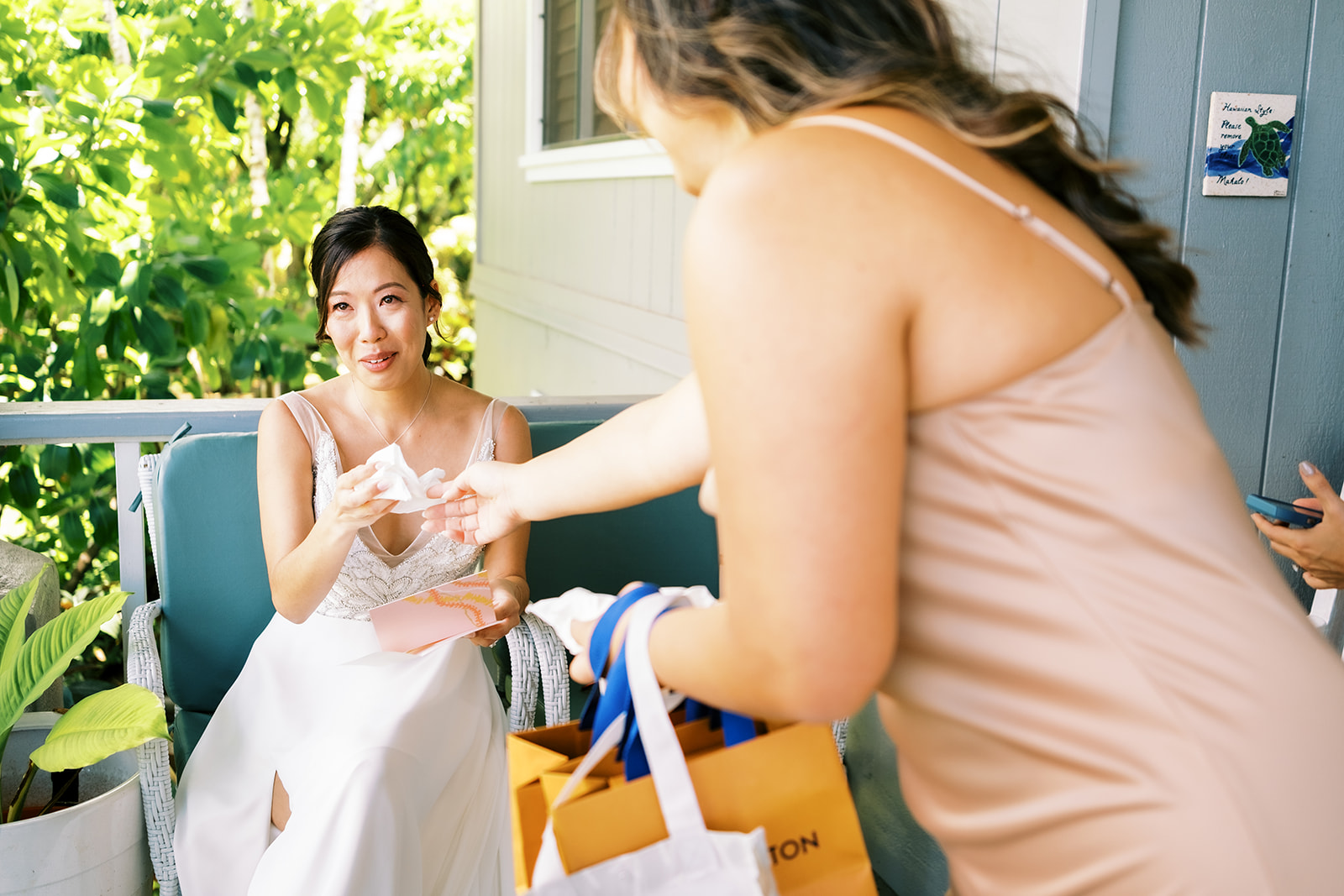 Bride sitting on a porch receiving a gift from a bridesmaid.
