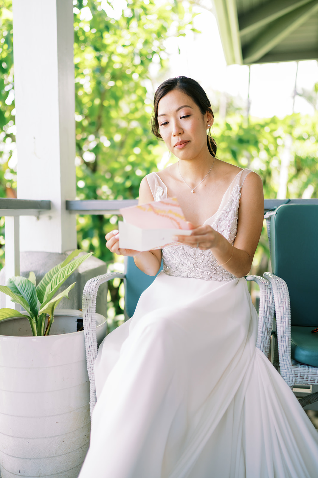 Bride in a white dress sitting on a patio holding a small pink gift box captured by Oahu Wedding Photographer