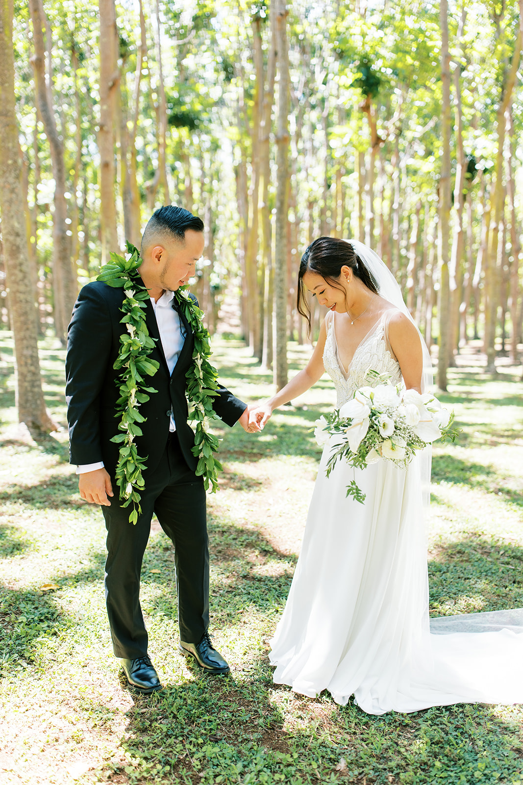 A couple in wedding attire exchanging a playful moment in a sunlit forest at Na Aina Kai  captured by Oahu Wedding
