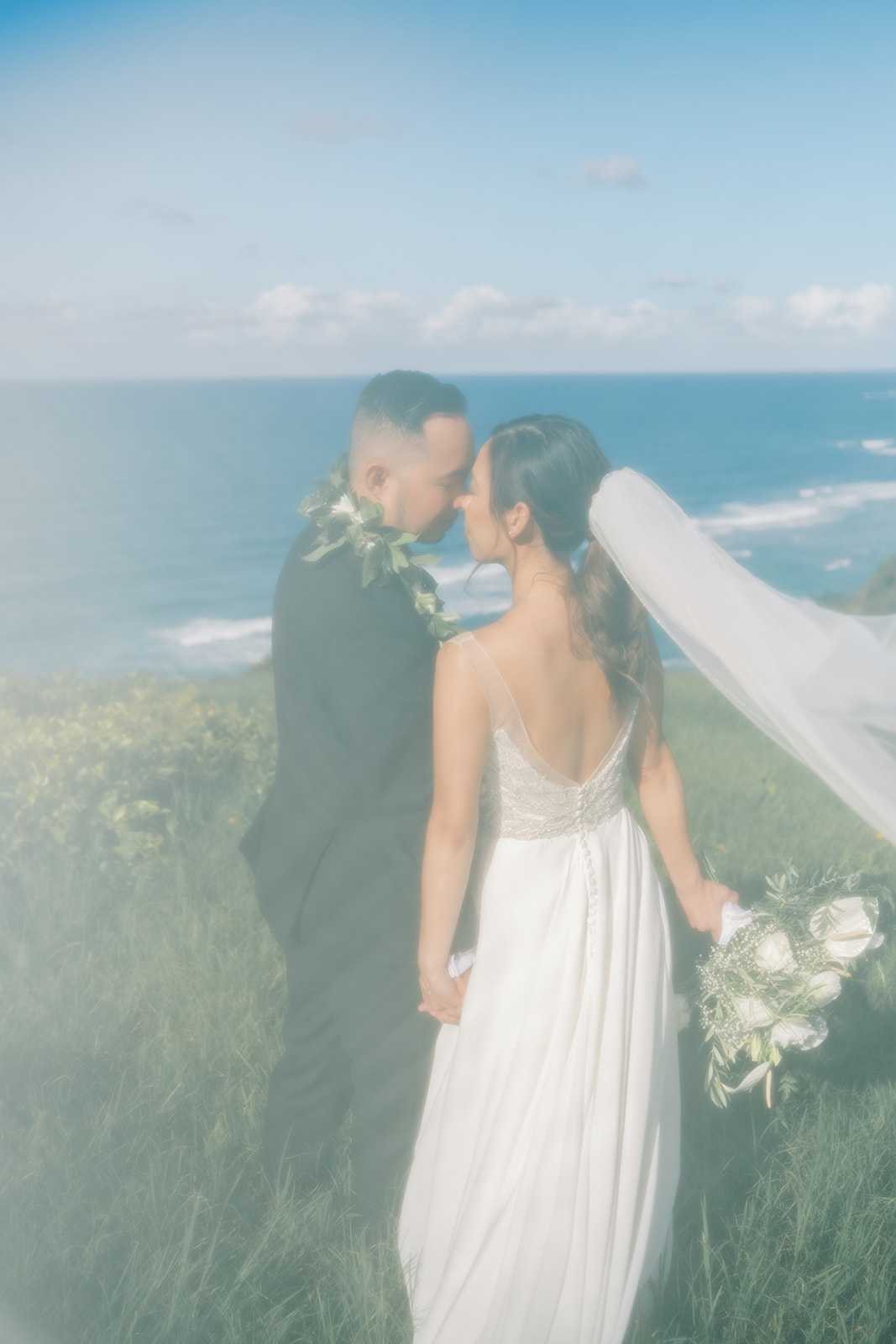 A couple in wedding attire sharing a kiss by the sea, with a soft-focus effect captured by Oahu Wedding Photographer