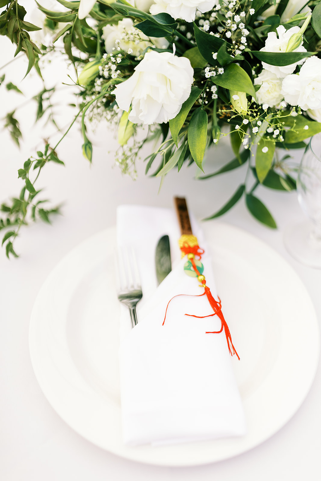 An elegant table setting with a white plate, silver cutlery, a white napkin, and a small floral decoration