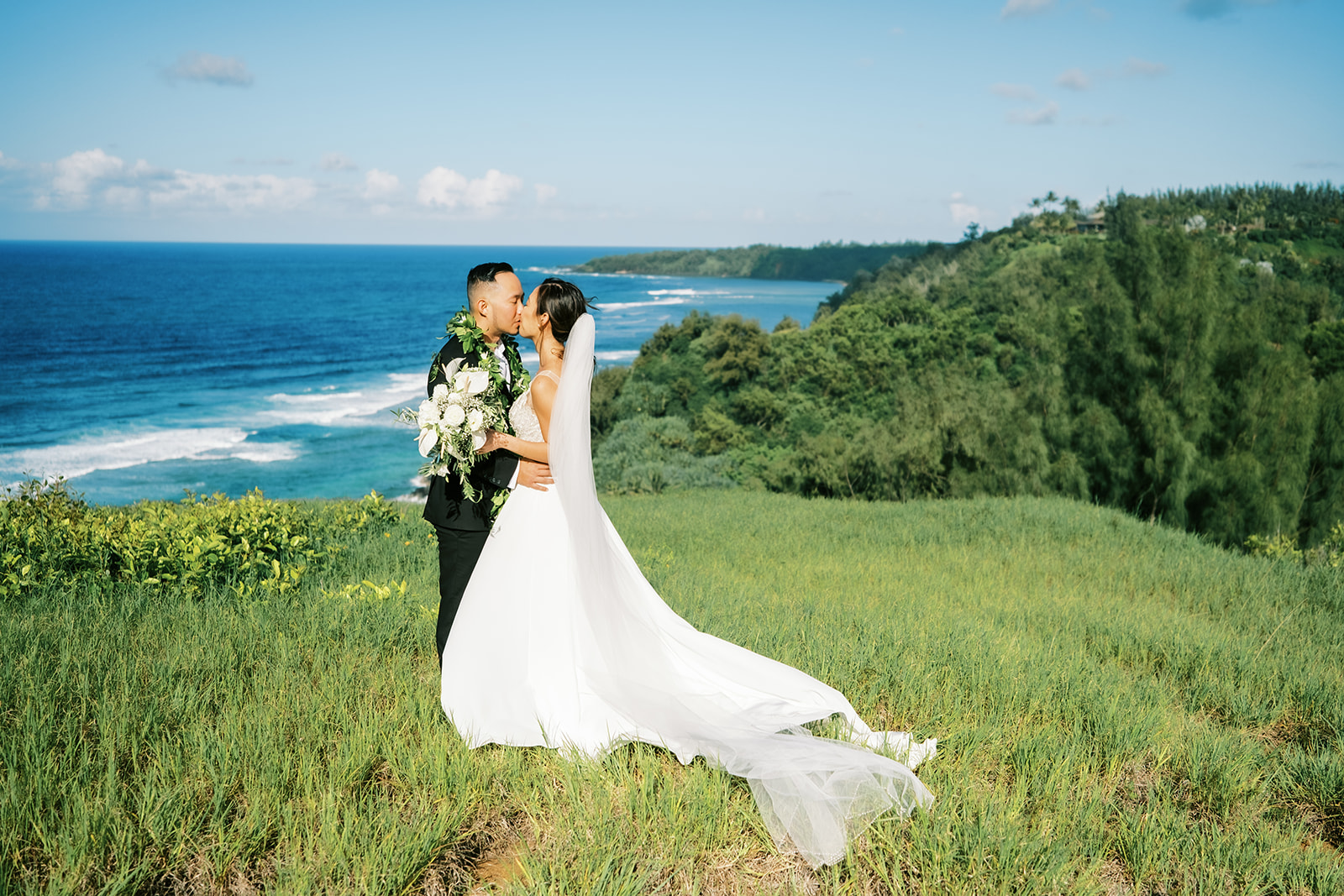 Newlyweds sharing a kiss on a grassy hill overlooking the ocean Wedding at Na Aina Kai takenby Oahu Wedding Photographer